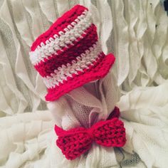 two crocheted hats with red and white bows on them sitting on a blanket