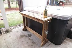 an outdoor hot tub with a wooden table next to it and a bottle of wine on top