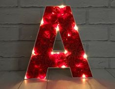 a lighted letter with roses on it sitting in front of a brick wall and floor