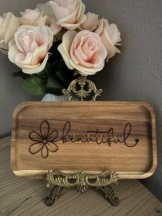 a wooden tray with the word beautiful on it next to some pink roses in a vase