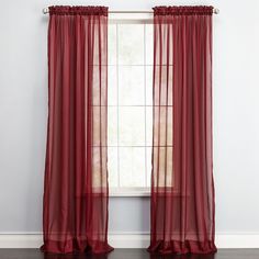 a window with red sheer curtains hanging from it's sides and a wooden floor