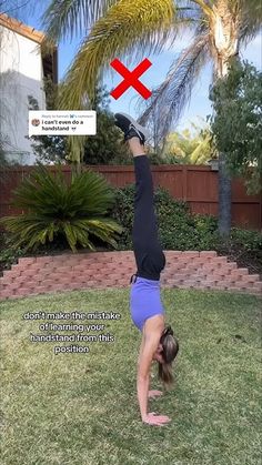 a woman doing a handstand in the grass with a red cross above her head