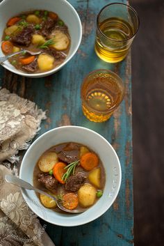 two bowls of beef stew with carrots, potatoes and celery next to a glass of beer