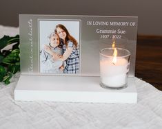 a candle is sitting next to a memorial card on a table with flowers and greenery