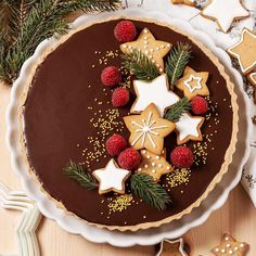 a chocolate tart decorated with christmas cookies, raspberries and star shaped biscuits