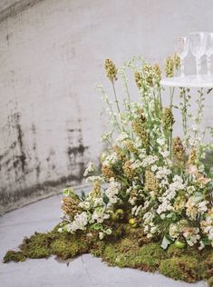 an arrangement of flowers and wine glasses sits on the ground in front of a concrete wall