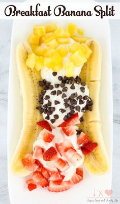 a banana split with strawberries, chocolate chips and cream in it on a white plate