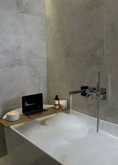 a bathtub with a laptop on it and candles in front of the tub's faucet