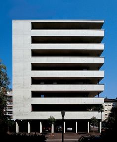 an apartment building with multiple balconies on the top and bottom floors, in front of a parking lot