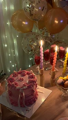 a table topped with a cake covered in frosting and lit candles next to balloons