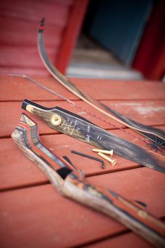 two different types of bow and arrow laying on a red wooden surface with the arrows still attached