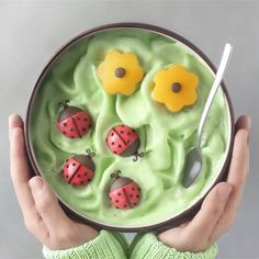 a person holding a bowl filled with green pudding and ladybugs on top of it