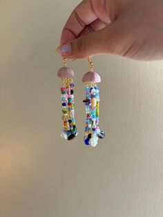 a pair of colorful beaded earrings being held by a woman's hand in front of a white wall