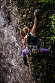 a woman climbing up the side of a mountain with her hands in the air while holding onto a rope