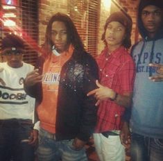 four young men standing next to each other in front of a brick wall and window