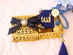 a gold box with a blue tassel and a name tag on it sitting next to some flowers