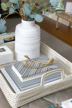 a white vase with some green plants in it and two trays on the table