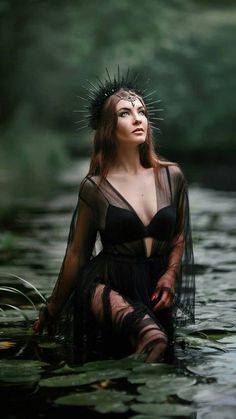 a woman in a black dress sitting on top of a body of water with plants