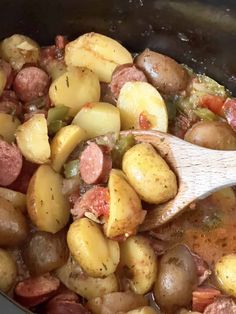 a pot filled with potatoes and sausage next to a wooden spoon