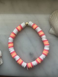 an orange and white beaded bracelet next to seashells on a marble counter