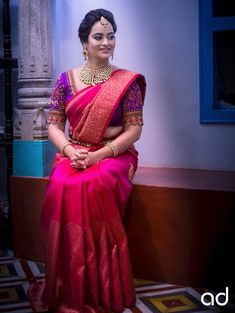 a woman in a red and gold sari sitting on a bench with her hands crossed