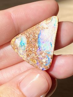 a hand holding a small triangle shaped piece of gold and blue material with white speckles