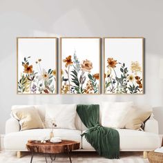 three floral paintings hanging on the wall in a living room with white furniture and green throw pillows