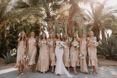 a group of women standing next to each other in front of palm trees and flowers