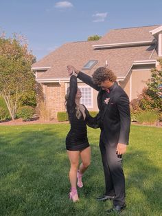 a man and woman dressed in black dancing on the grass outside their house with balloons