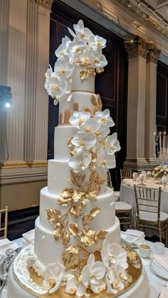 a large white and gold wedding cake with flowers on it's tiers in a banquet room