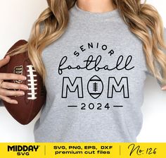 a woman holding a football and wearing a shirt that says senior football mom on it