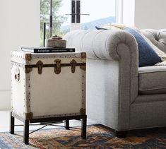 an old trunk sitting on top of a table in front of a couch with pillows