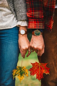 two people holding hands with autumn leaves on their fingers and watch in the other hand