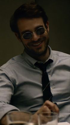 a man wearing glasses and a tie sitting at a table with a drink in front of him