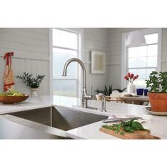 a kitchen sink sitting under a window next to a cutting board and potted plant