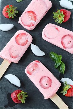 strawberry ice cream popsicles on a black tray with spoons and strawberries in the background