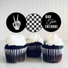 three cupcakes with black frosting and white icing on top, one has a hand sign that says bad two the bone