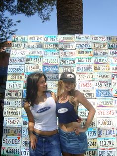 two young women standing next to each other in front of a wall covered with license plates