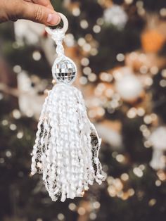 a hand holding a glass ornament in front of a christmas tree