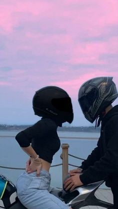 two people sitting on a motorcycle with their helmets on and one person wearing a helmet