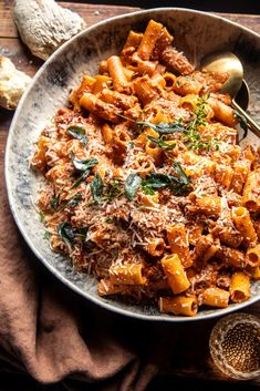 a bowl filled with pasta and sauce on top of a wooden table next to bread