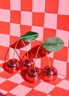 three shiny red cherries with green leaves in front of a checkered wall and floor