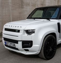 a white land rover is parked in front of a concrete wall with black rims