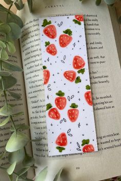 a bookmark with strawberries on it sitting next to some leaves and an open book