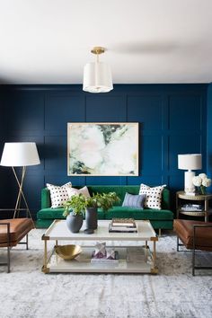 a living room with blue walls and green couches in the center, along with two lamps on either side of the coffee table