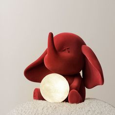 a small red elephant sitting on top of a white pillow with a light in it's trunk