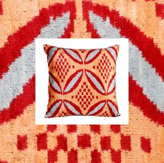 an orange, red and grey pillow with a white square in the middle on a multicolored area rug