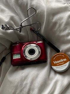 a red camera sitting on top of a bed next to a white blanket and a brown button