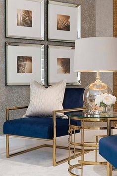 a living room with two blue chairs and a gold coffee table in front of three framed pictures