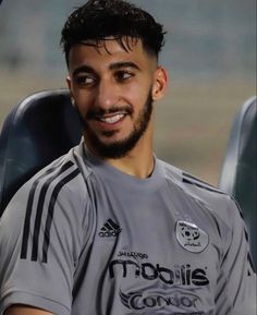 a man sitting in a chair wearing a soccer uniform and looking at the camera with a smile on his face